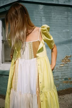 a woman standing in front of a blue building wearing a yellow and white dress with ruffles