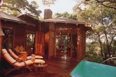 a wooden deck with chairs and a hot tub in front of a tree - lined house