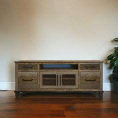 a wooden entertainment center sitting on top of a hard wood floor next to a potted plant