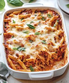 a casserole dish filled with pasta and meat, topped with fresh basil leaves