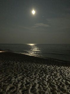 the moon is shining over the ocean on a beach