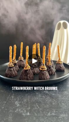 chocolate covered strawberries with brooms on a black plate next to a white ghost