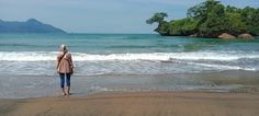 a woman standing on top of a sandy beach next to the ocean with an island in the background