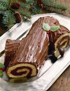 a chocolate roll cake on a silver platter next to pine cones and greenery