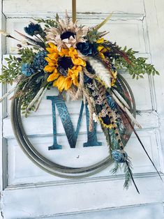 a wreath with sunflowers, feathers and the letter m is hanging on a door