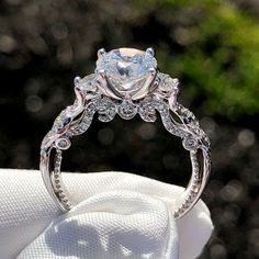 a close up of a diamond ring on top of a white cloth with trees in the background