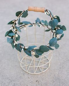 a white wire basket with green leaves and a wooden handle sitting on the concrete floor