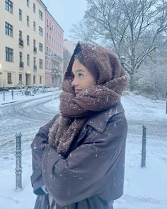 a woman is standing in the snow with her head covered by a scarf and jacket