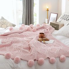 a pink blanket with pom - poms on it is laying on a bed