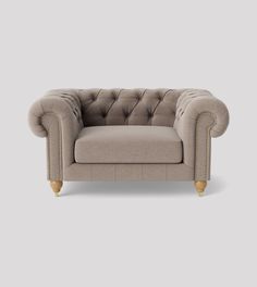 a grey couch with wooden legs and buttons on the back, in front of a gray background