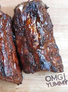 two pieces of meat sitting on top of a cutting board with the word omg yummy written below it