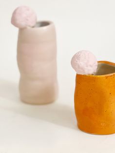 two small vases with cotton balls in them sitting next to each other on a white surface