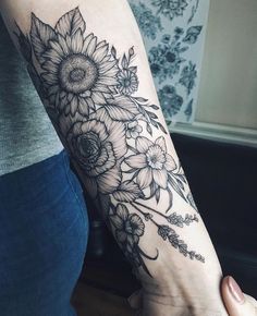 a woman's arm with sunflowers and leaves tattoo on her left arm