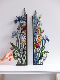 two pieces of art made out of paper with flowers and plants painted on the sides