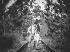 a man and woman standing on train tracks in the middle of some trees with their arms around each other