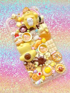 a phone case with various candies and teddy bears on it sitting on a glitter background