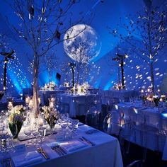 a table set up with white linens and silverware, lit by blue lights