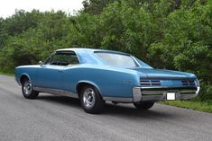 an old blue car is parked on the side of the road in front of some trees