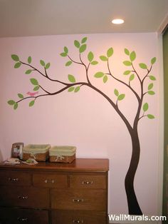 a tree with green leaves painted on the wall next to a dresser in a child's room