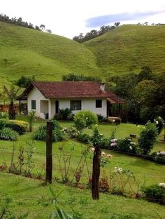 a white house sitting in the middle of a lush green field next to a hill