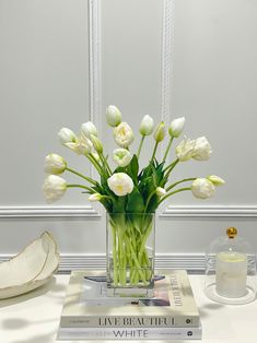 a vase filled with white tulips on top of a table next to a stack of books