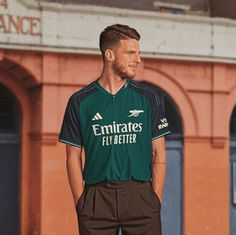 a man standing in front of a building wearing a green and black shirt with emirates fly better written on it