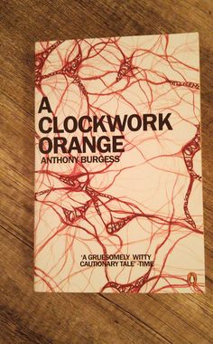 a clockwork orange book sitting on top of a wooden table next to a cell phone