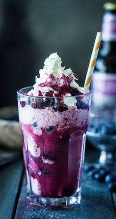 an ice cream sundae with blueberries and whipped cream in a glass on a table