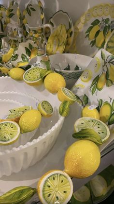 lemons and lime slices are on display in front of dishes with green leaves around them