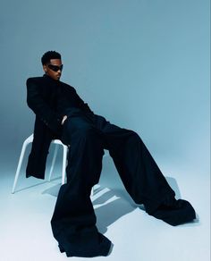 a man sitting on top of a white chair next to a black suit and sunglasses