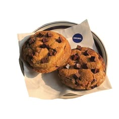 two chocolate chip cookies sitting on top of a white paper wrapper next to each other