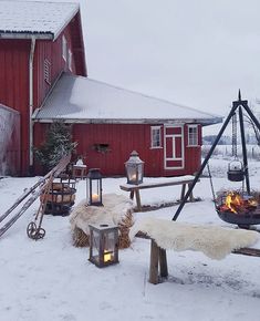 an outdoor fire pit in the snow next to a red barn with candles on it