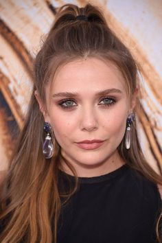 a close up of a person with long hair wearing earrings and a black top shirt