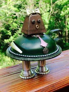 a green metal tea pot with a bow on it's head sitting on top of a wooden table