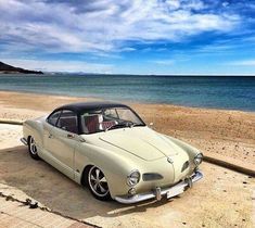 an old car is parked on the beach by the water's edge in front of some blue skies