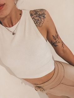 a woman with tattoos on her arm and leg, sitting in front of a white wall