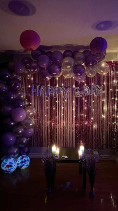 balloons and streamers are hanging from the ceiling in front of a table with candles