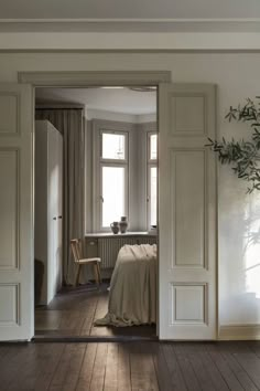 an open door leading to a bedroom with white walls and wood flooring in front of a window