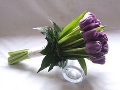 a bouquet of purple tulips in a glass vase on a white tablecloth