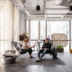 a man and woman sitting on chairs in an open room with hanging lights above them