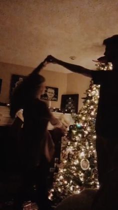 two people standing in front of a christmas tree with their arms out to each other