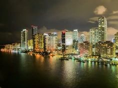 an aerial view of a city at night with lights reflecting off the water in front of it