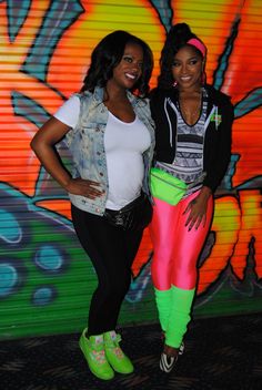 two women standing next to each other in front of a graffiti wall