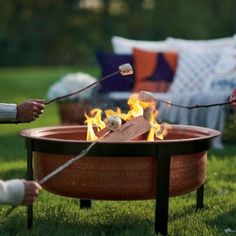 two people are pulling a stick over an outdoor fire pit that has flames coming out of it