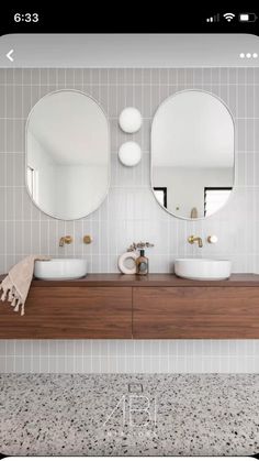 two round mirrors on the wall above sinks in a white tiled bathroom with wood cabinets