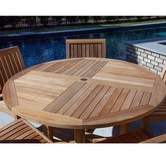 a wooden table with four chairs around it near a swimming pool and brick wall in the background