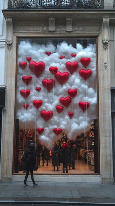 a person walking in front of a store with red and white heart balloons attached to it