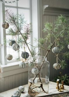 a christmas tree in a glass vase with ornaments hanging from it's branches on a table