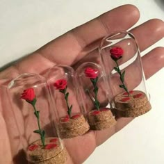 four tiny red roses are placed inside small glass vases in the palm of someone's hand