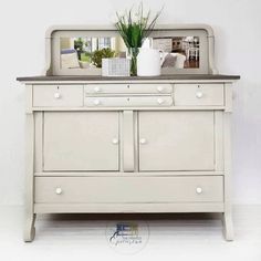 a white dresser with a mirror on top of it next to a potted plant